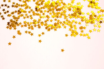 Obraz na płótnie Canvas Gold sequins in the shape of stars shimmer on a pink background. Backgrounds with copyspace for a holiday, party decoration, Christmas and new year, birthday and anniversary. Gradient and texture