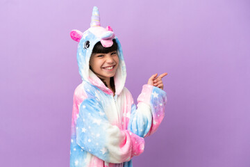 Little kid wearing a unicorn pajama isolated on purple background pointing finger to the side © luismolinero