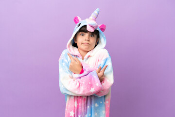 Obraz na płótnie Canvas Little kid wearing a unicorn pajama isolated on purple background pointing to the laterals having doubts