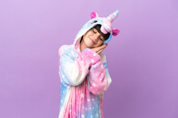 Little kid wearing a unicorn pajama isolated on purple background making sleep gesture in dorable expression