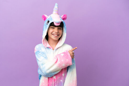 Little kid wearing a unicorn pajama isolated on purple background pointing to the side to present a product