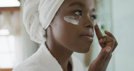 Portrait of african american attractive woman applying face cream in bathroom - Powered by Adobe