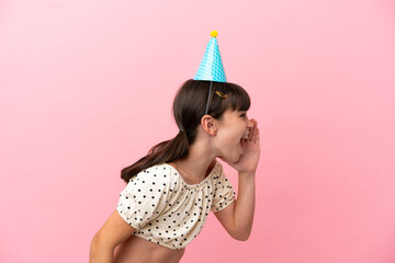 Little caucasian kid with birthday hat isolated on pink background shouting with mouth wide open to...