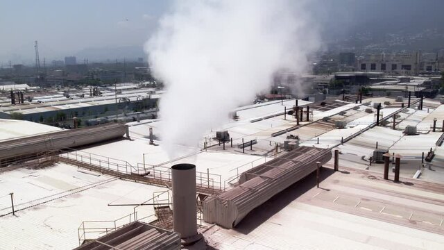 Una chimenea con humo blanco de vapor de agua sale de una industria en medio de una ciudad