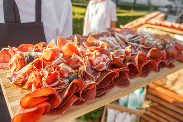 On the table there is a slicing of raw smoked sausage, ham, raw smoked meat with olives on a wooden tray.