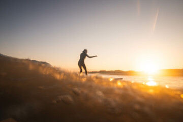 Fototapeta na wymiar A woman surfer catches a wave at sunrise