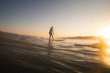 A woman surfer catches a wave at sunrise
