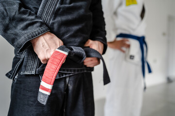 Side view of hand of unknown caucasian man in kimono gi standing while holding black bjj belt brazilian jiu jitsu concept copy space - obrazy, fototapety, plakaty