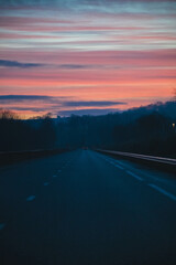 Fototapeta premium A sunrise over a lonely road with a single car