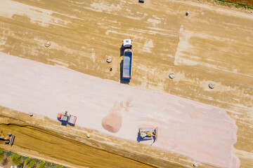 Aerial photo of bulldozer pours sand into the truck. On the cons