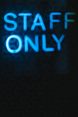 Blurred neon letters, signboard staff only on a black wall close-up.