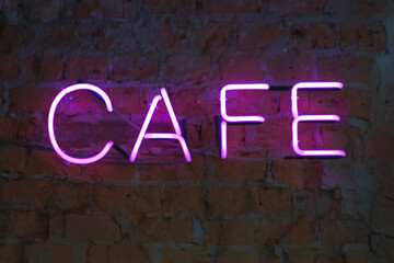 Neon letters, bright signboard cafe on a brick wall close-up.