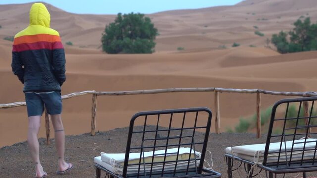 Man wears short and a rain jacket in desert near unusable sunbed on a