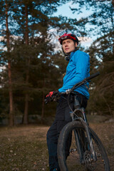 Man wearing bicycle helmet standing in forest, spending free vacation time on a bicycle trip in a forest.