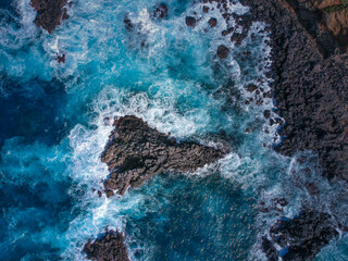 Aerial top view of sea waves hitting black volcanic rocks