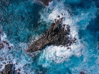 Aerial top view of sea waves hitting black volcanic rocks