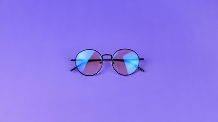 Glasses with a blue light filter to protect the eyes while working at the computer. Round glasses for filtering blue light. Stylish round glasses on a purple background, top view.
