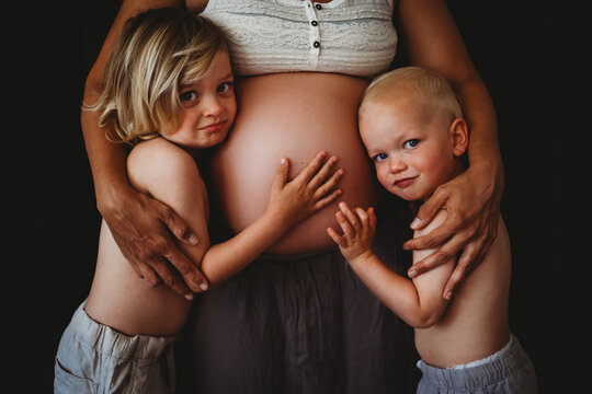 Young boys touching mom's pregnant big belly looking at camera