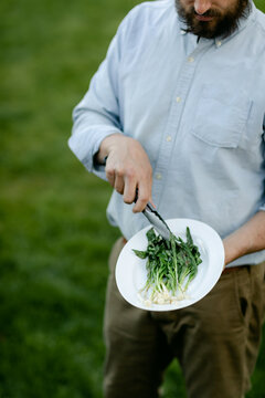 Vertical photo of man using tongs to toss the wild ramps on a platter