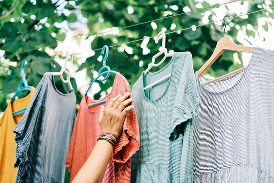 Woman hangs colorful dresses on hangers on clothesline in home garden