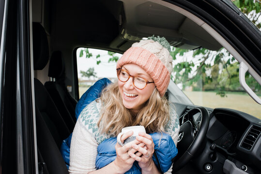 woman sat in her camper van laughing joyfully whilst drinking coffee