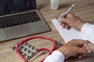 Doctor working with laptop and writing on paper