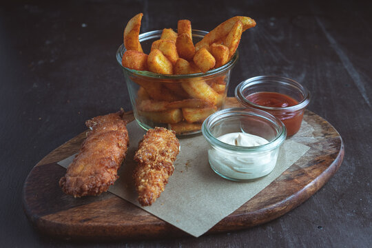 Two chicken strips in batter with french fries on a wooden board