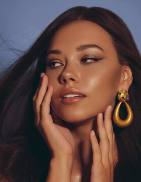 Beautiful Woman Smooth Long Hair Brunette Evening Make Up With Liner Tanned Skin Beautiful Female Portrait Over Blue Background Wearing Gold Earrings