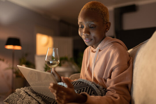 Black woman with wine and tablet resting at home