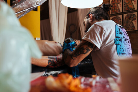 Back view of tattoo artist working on a customer's arm in his studio.