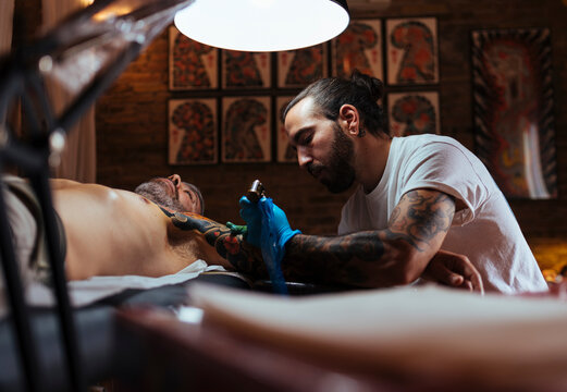 Side view of tattoo artist working on a customer's arm in his studio.