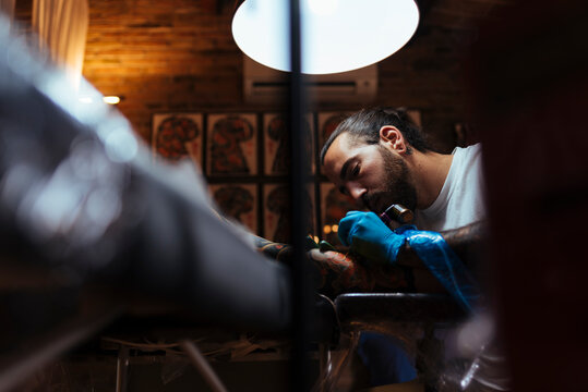 View under of tattoo artist working with a customer in his studio.