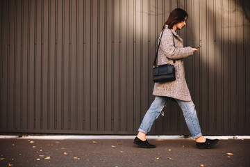 Side view of non-binary woman using smart phone walking against wall