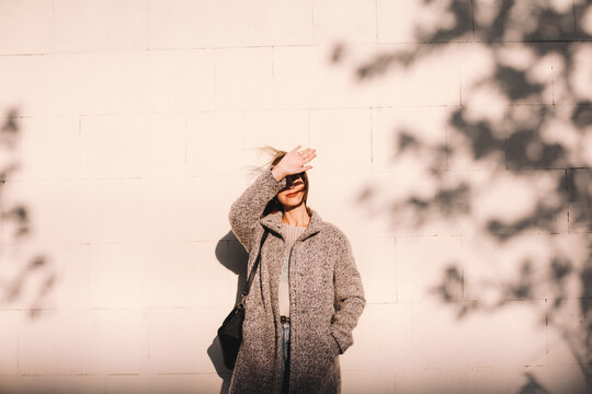 Young woman shielding eyes standing against wall in city