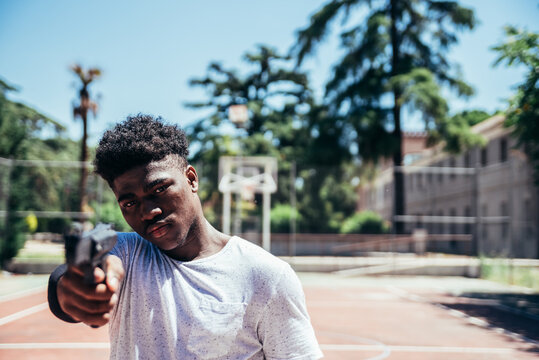 Black African American boy on a basketball court aiming a gun at camera