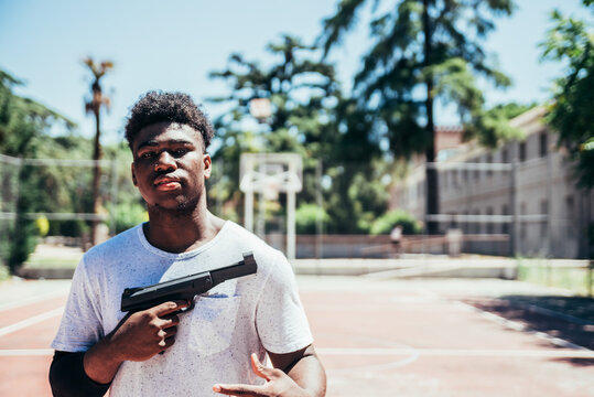 Black African American boy clutching a gun on an urban basketball court.