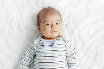 Two months newborn Asian Chinese baby boy lying on his back on bed.