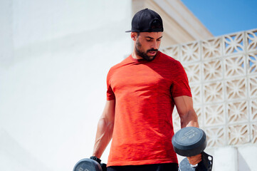 Muscular young man lifting weights outside