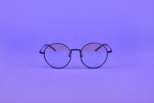 Glasses with a blue light filter to protect the eyes while working at the computer. Round glasses for filtering blue light. Stylish round lenses on a purple background, top view.