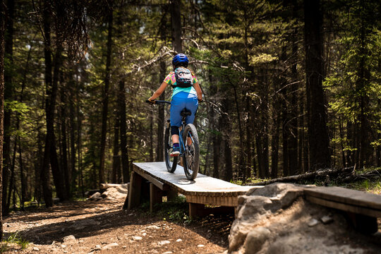 A female cyclist rides her mountain bike down a wooden ramp on the Top Notch cycling trail on Tunnel Mountain. - Powered by Adobe