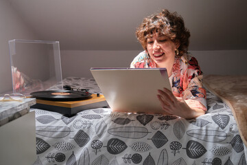 Young woman laying on her bed, listening a vinyl record and looking at the sleeve