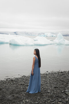 Asian young woman standing near melting ice glacier lake Jokulsarlon in Iceland in long blue dress