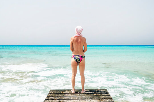 Woman in swimsuit with pink scarf on the beach, has cancer