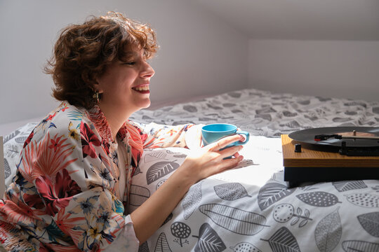 Young hipster girl listening music on a turntable, smiling and drinking coffee