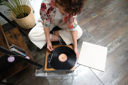 Young woman playing a vinyl record on a turntable at home - Powered by Adobe