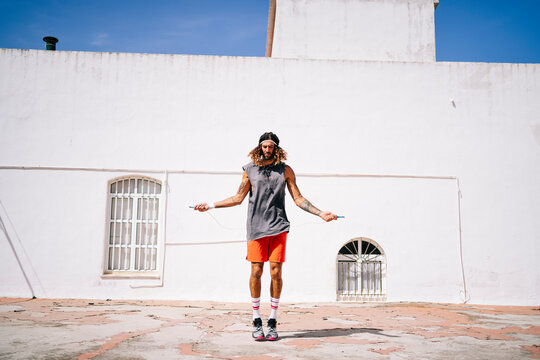 Long-haired athlete man skipping rope outdoors
