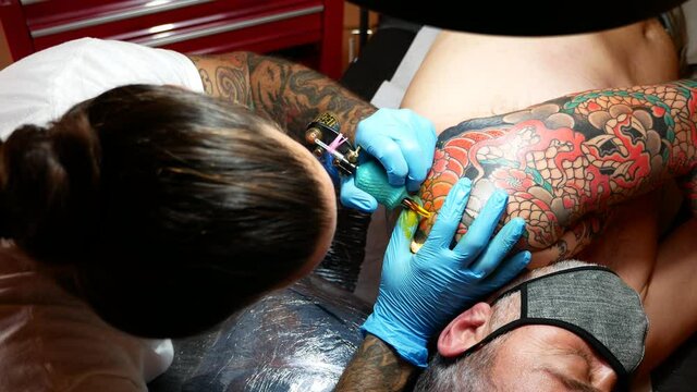 Aerial view of an tattoo artist working on a customer's arm.
