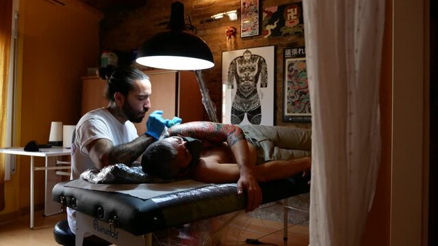 View of tattoo artist working on a customer's arm in his studio.