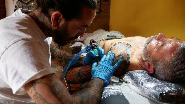 Side view of tattoo artist working on a customer's arm in his studio.