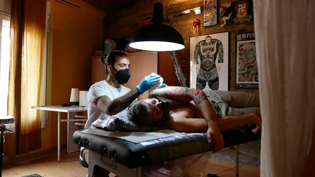View of tattoo artist working on a customer's arm in his studio.